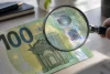 Billet de 100 euros examiné à la loupe pour contrôler ses signes de sécurité.